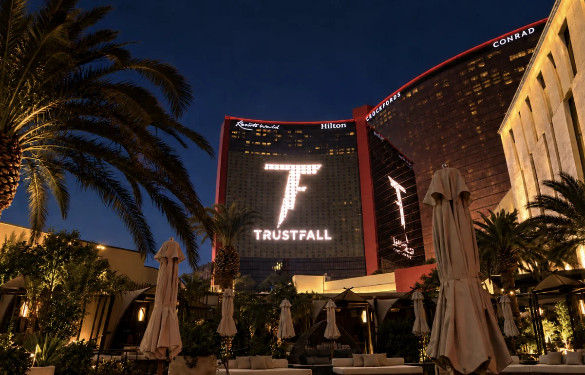 Resorts World Las Vegas tower at night with the illuminated Trustfall logo on its facade, framed by palm trees
